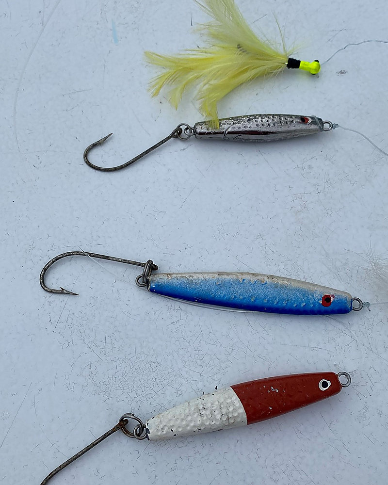 Three jigs laid out on the deck: a bucktail, a blue metal jig and a red and white jig