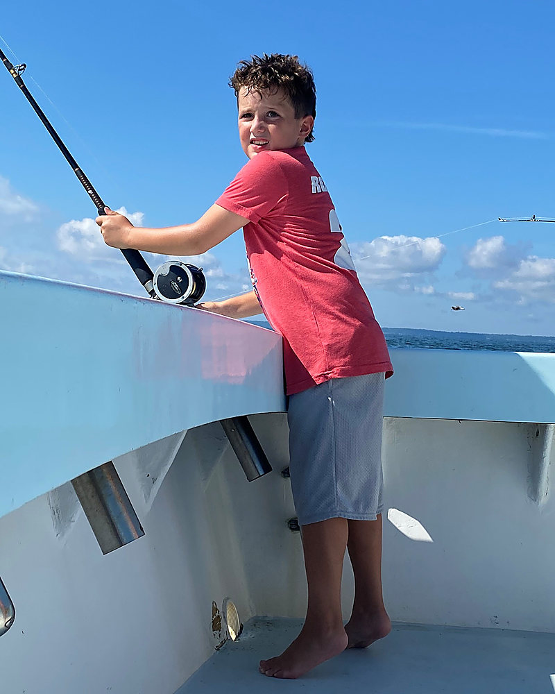 A boy leaning on the rail with a trolling rod