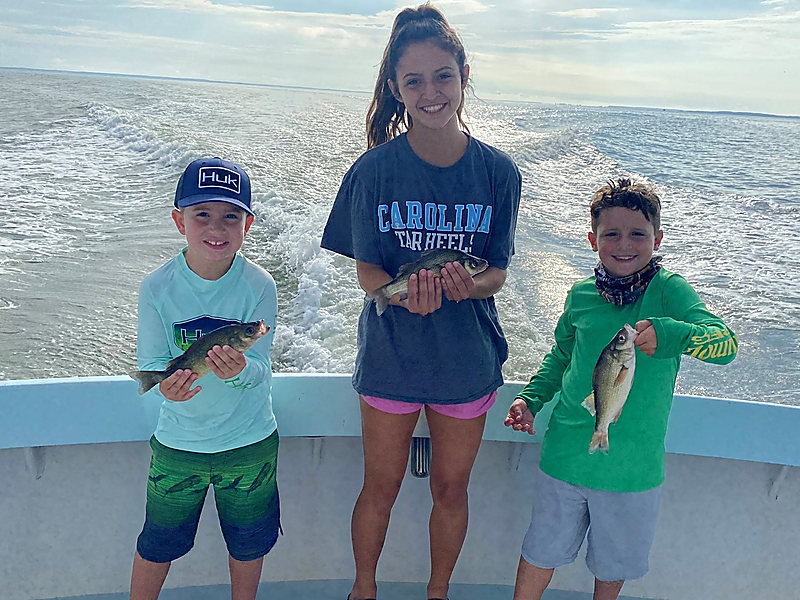 Three kids on the stern, each holding a fish